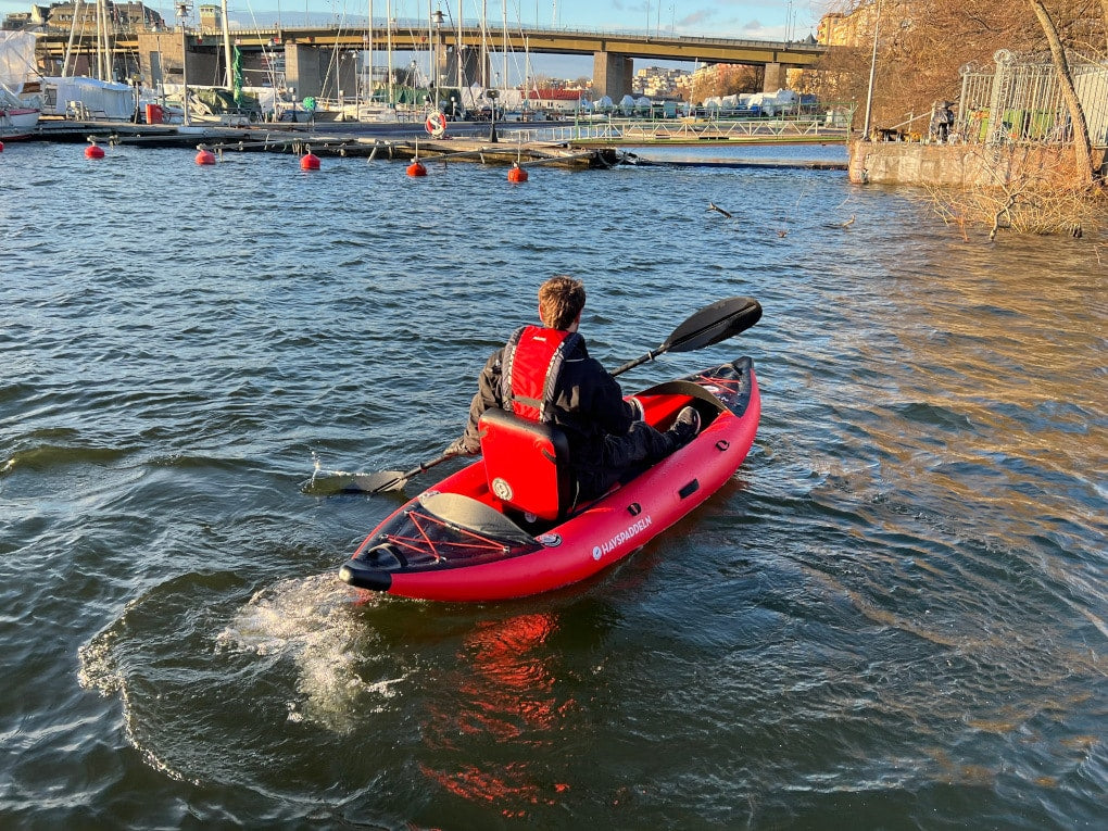 Person paddlar Havspaddeln Frej – en svart och röd uppblåsbar kajak, i öppet vatten.